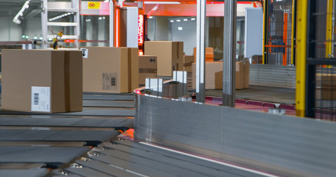 Cardboard Parcels, Boxes, Packages are Transported on an Automated Conveyor Line in a Busy Sorting Center at a Postal Service Warehouse. Concept of Logistics and Shipping Operations - Powered by Adobe