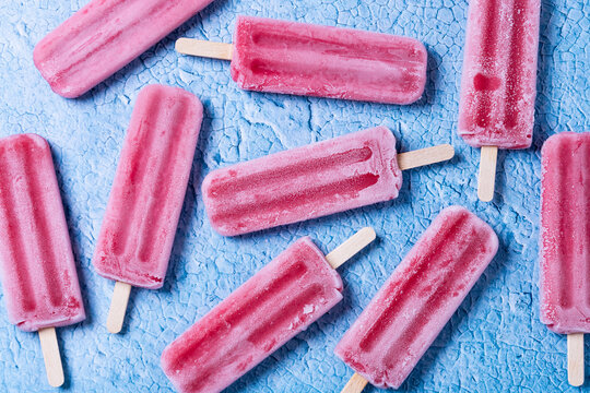 Red strawberry popsicles pattern on blue background. Top view