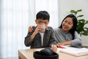 Hydration and Comfort. A mother encourages her son to take a break and hydrate while studying at...