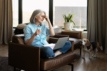 Stressed senior woman having headache while working from home with laptop