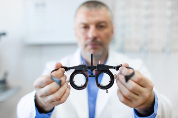 Professional male optometrist at work, holding an optometer, with an eye check chart in the...