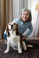 Happy senior woman playing with beagle dog at home
