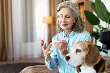 Senior woman testing blood glucose at home with her dog