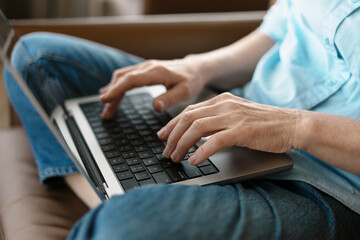 Fototapeta premium Senior woman typing on laptop keyboard while sitting comfortably on sofa