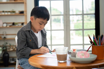 Creative Moments and Learning. A young boy focused on drawing at the table.