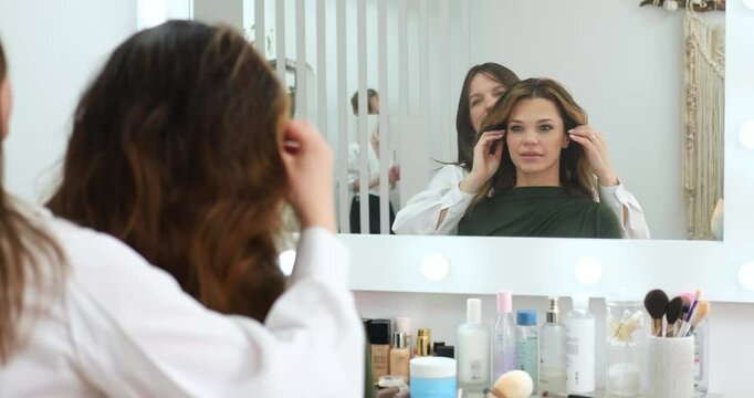 A woman is seated in beauty salon, getting her hair styled by skilled hairdresser while looking at her reflection in mirror, self care, beauty routine, salon experience