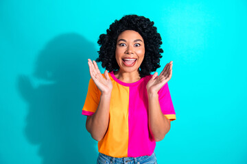 Joyful young woman expressing excitement in a color block t-shirt on a vibrant teal background with...