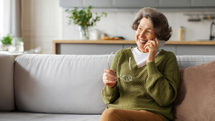 Happy modern senior woman talking on cellphone and smiling, enjoying conversation, sitting in her...