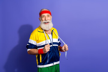 Happy senior man in retro sportswear practicing fitness with measuring tape on purple background