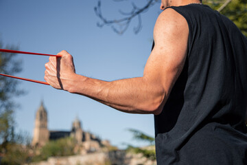 Close-up of male arm pulling red resistance band during outdoor workout in Salamanca, Spain with blurred historic architecture in the background