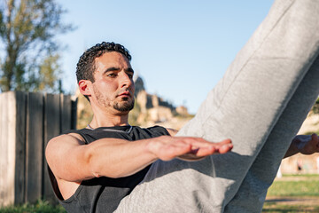 Focused man holding V-sit core position outdoors on sunny day, showcasing strength, balance, and...