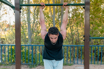 Close-up of athletic man hanging from outdoor fitness bar, emphasizing arm strength, stability, and engagement in upper body during bodyweight routine