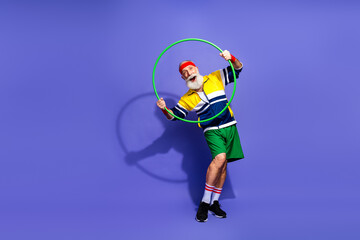 Obraz premium Elderly man in colorful retro sportswear performing with a hula hoop against vibrant blue background