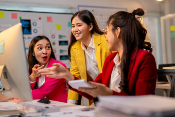 Three women are sitting at a desk with a computer monitor in front of them