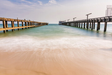 Fototapeta premium Rustic parallel piers stretch out into the ocean with gentle waves washing onto the sandy beach under a partly cloudy sky