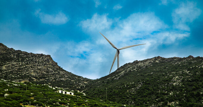 A large wind turbine stands between two green mountains under a blue sky, symbolizing renewable energy in the heart of the Moroccan landscape.