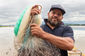 Portrait of a colombian artisanal fisherman holding a cast net and looking at the camera on the...