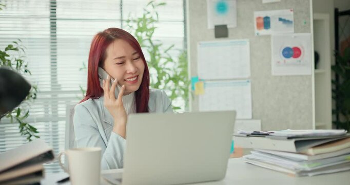 Young busy asian business woman working on project paperwork talking phone, using laptop remotely work in modern office. Female freelancer entrepreneur making distance job telesale call with customer.