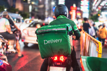 Motorcycle food courier wearing green uniform and delivery backpack navigating crowded urban street...