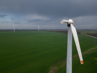 Close-up of a damaged wind turbine blade on a large green field with multiple turbines and cloudy...