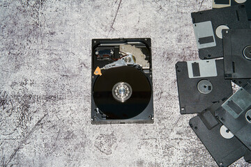 An open 3.5 inch hard disk drive alongside multiple floppy disks on a gray surface.