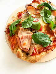 Delicious homemade pizza with tomatoes, ham, and fresh spinach