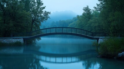 A misty arched bridge over calm water and lush green trees