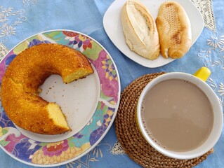 Café-da-manhã com bolo de milho, café com leite e pão francês.