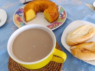 Café-da-manhã com bolo de milho, café com leite e pão francês.