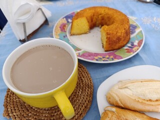Café-da-manhã com bolo de milho, café com leite e pão francês.