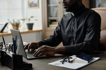 Medium shot of African American pastor typing on laptops keyboard while sitting at table with...