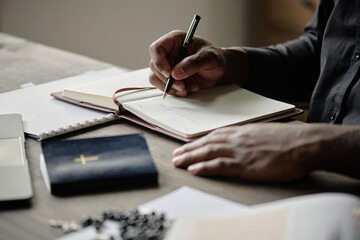 Medium close up of unrecognizable pastor holding pen while writing in notebook in office during workday