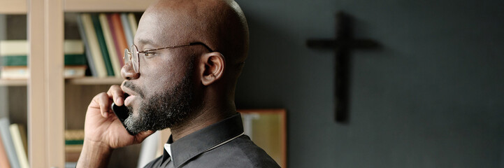 Website banner of African American pastor talking on smartphone while standing in front of window...