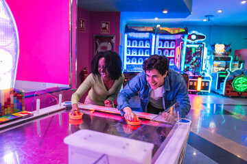 Two friends enjoying a competitive game of air hockey, surrounded by the vibrant lights and atmosphere of an entertainment venue