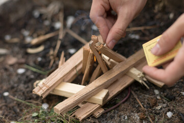 Teenagers light a campfire using wooden kindling and matches, engaging in a classic outdoor skill that encourages teamwork, responsibility, and connection with nature.