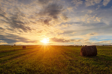 Scenic sunset over hay bales in a field. Golden light bathes the landscape, creating a tranquil scene. For agriculture, travel and inspiring greeting card designs.