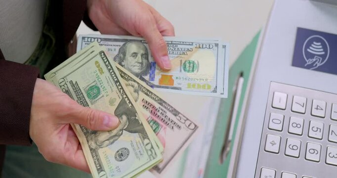 Person holds US dollar bills near ATM or payment terminal keypad