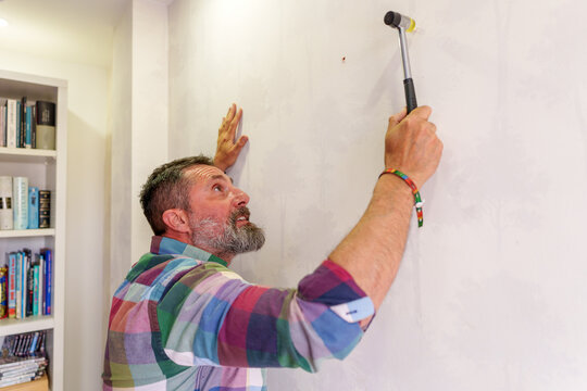 Skilled professional driving nail into wall, repairing interior space with precision woodworking tools