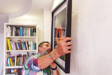Fototapeta premium Interior designer hanging a framed painting of a solar eclipse on a white wall in a modern living room
