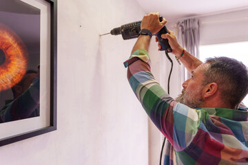 Professional handyman drilling precise hole in white wall, preparing to hang decorative artwork...