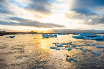 Golden sunset casts a warm glow over an Arctic landscape, highlighting iceberg formations in serene...
