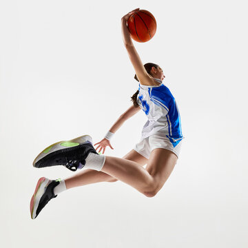 Low angle view of young athletic teen girl scoring winning goal in motion with powerful spam dunk against white background. Concept of professional sport, woman in sport, movement, fitness. Ad