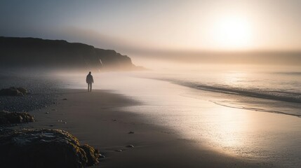 A solitary figure walks along a misty and sandy beach coastline