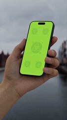 GREEN SCREEN CHROMA KEY Hand holds smartphone by the riverside with historic buildings in the background on an overcast day, ideal for customizable app or branding content