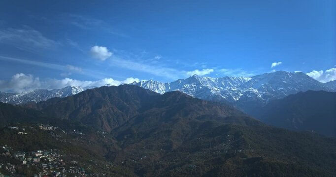 A hyperlapse aerial shot of Dharamshala&rsquo;s Dhauladhar mountains, showcasing snow-clad peaks glowing in the morning sun with swiftly drifting clouds above.