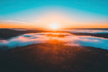 Sunrise over a valley shrouded in colorful morning mist  Aerial view of a landscape with vibrant colors  Sunrise paints the fog with golden hues, revealing forest below