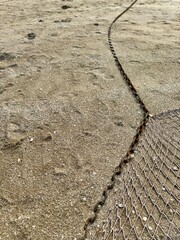 A fishing net with a rusted chain lies on coarse sandy ground, curving into the distance, with...