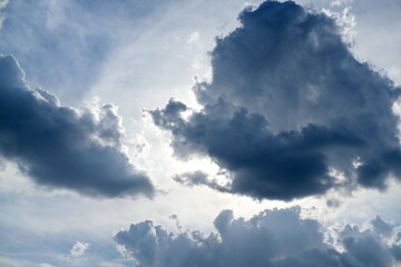 Obraz premium Dramatic sky filled with large dark clouds, partially covering the sun. Bright light breaks through the gaps, creating a powerful contrast between shadow and illumination, evoking a moody atmosphere.