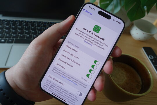 Kiel, SH, Germany, 04-24-2025: User navigating Face ID settings on an iPhone with a coffee mug and laptop in the background