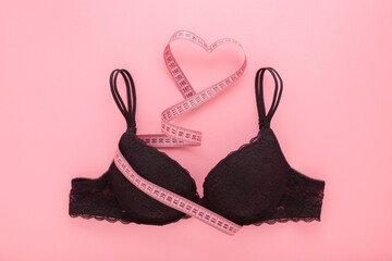 Heart shape created from measure tape and dark black lace bra on light pink table background....